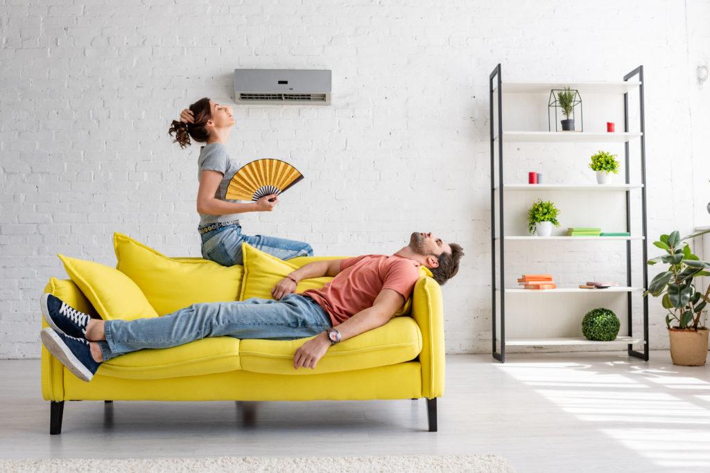 exhausted man lying on yellow sofa under air conditioner near wo