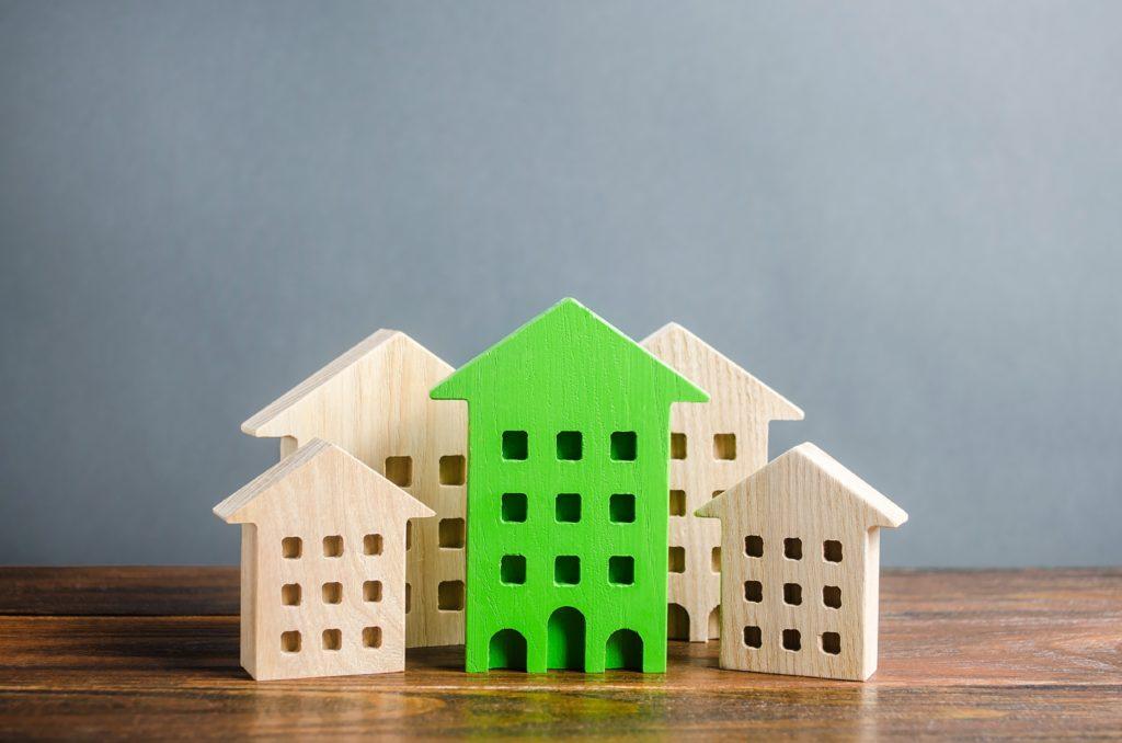 Green figure of a residential building stands out among the rest of the houses. Search for the best option to buy an apartment. High quality and convenient location. eco-friendly and energy saving