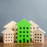 Green figure of a residential building stands out among the rest of the houses. Search for the best option to buy an apartment. High quality and convenient location. eco-friendly and energy saving