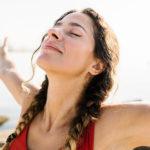 Young adult hispanic woman breathing fresh air standing on the beach at summer - Portrait of sportive hispanic female relaxing by the sea - Wellness and healthcare lifestyle concept
